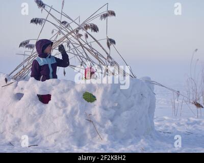 Girls playing in snow fortress on frozen lake during cold winter day Stock Photo