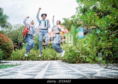 three Indonesian high school students jumped in their school bags raising their hands together Stock Photo