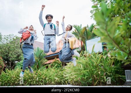 three high school students jumping high wearing school bags raising their hands together Stock Photo
