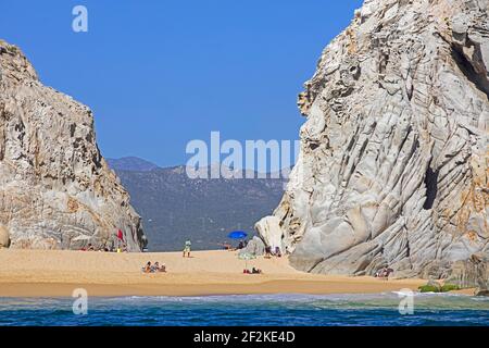 Limestone sea cliffs and tourists sunbathing on secluded beach near the seaside resort Cabo San Lucas on the peninsula of Baja California Sur, Mexico Stock Photo