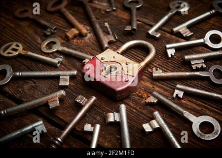Vintage rusty padlock surrounded by group of old keys on a weathered wooden background. Internet security and data protection concept, blockchain and Stock Photo