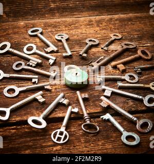 Vintage rusty padlock surrounded by group of old keys on a weathered wooden background. Internet security and data protection concept, blockchain and Stock Photo