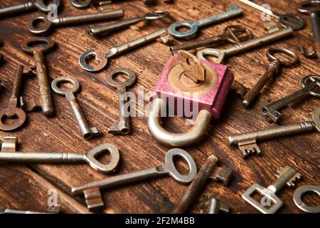 Vintage rusty padlock surrounded by group of old keys on a weathered wooden background. Internet security and data protection concept, blockchain and Stock Photo