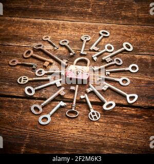 Vintage rusty padlock surrounded by group of old keys on a weathered wooden background. Internet security and data protection concept, blockchain and Stock Photo