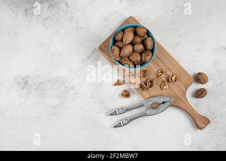 Blue bowl of whole walnuts on wooden cutting board Stock Photo