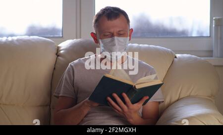 Man at home on the sofa reading a book, self-isolation, window background Stock Photo