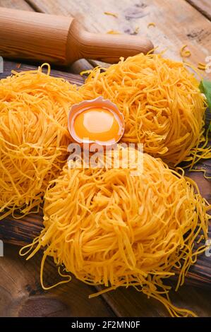 Tagliatelle pasta is thin. Traditional Italian named Angel Hair. Italian egg pasta, homemade and fresh on a wooden table. Rustic cuisine of the north of Italy. Copy space. Vertical photo Stock Photo
