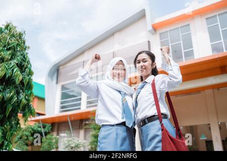 two beautiful student wearing an Indonesian high school uniform and bag with raise hands Stock Photo