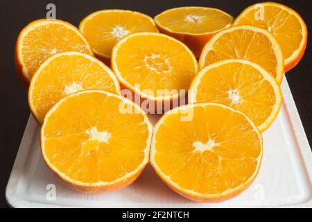 Nice composition of fresh oranges cut in half on a white cutting board on the dark kitchen table. Preparation of healthy juices. Stock Photo
