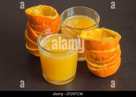 Two glasses of freshly squeezed orange juice with the fruit peels next to them on an elegant dark wooden table. Healthy food with citrus. Stock Photo