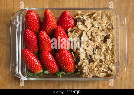 Rectangular transparent glass dish filled with strawberries and wheat cereals with chocolate on a wooden table. Healthy breakfasts. Stock Photo