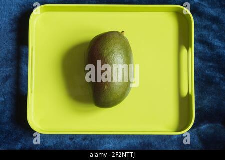 A large green mango on a colorful tray with space to input a text. Tropical fruits and food. Stock Photo