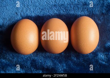 Close-up of three brown eggs together on a textured blue background. Farm food. Stock Photo
