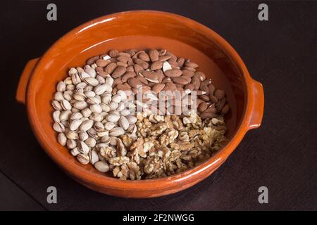 A group of walnuts, pistachio, and almonds scattered neatly on a wooden casserole on a dark table. Variety of nuts. Stock Photo