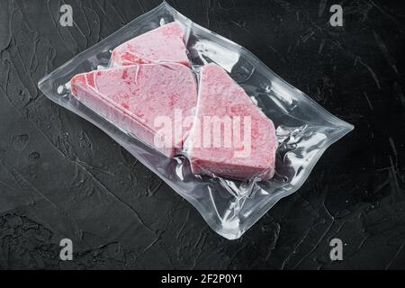 Raw frozen tuna fillet in vacuum packaging set, on black stone background , with copyspace and space for text Stock Photo