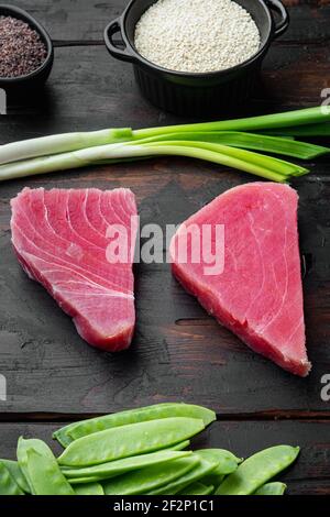 Raw tuna steak, fresh red tuna fillet with ingredients, green pea, sesame and spices set, on old dark wooden table background Stock Photo
