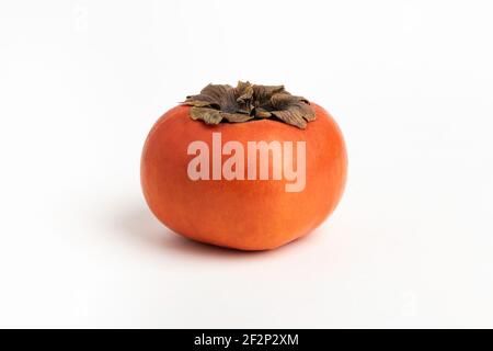 Close-up shot with shallow depth of field of a ripe persimmon fruit set on a plain white background. Stock Photo