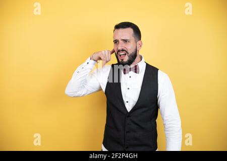 Young man with beard wearing bow tie and vest smiling doing phone gesture with hand and fingers like talking on the telephone Stock Photo