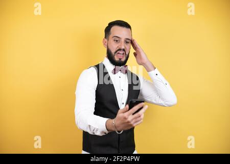 Young man with beard wearing bow tie and vest surprised looking through a magnifying glass Stock Photo