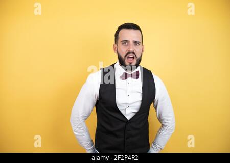 Young man with beard wearing bow tie and vest afraid and shocked with surprise and amazed expression, fear and excited face. Stock Photo