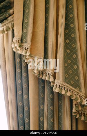 Expensive green and gold curtains with bells close up. Floral fringed curtains at the hotel. Stock Photo