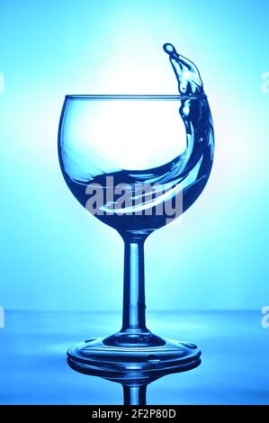 Glass of Water with splash on blue background. Beverage with splash. Stock Photo