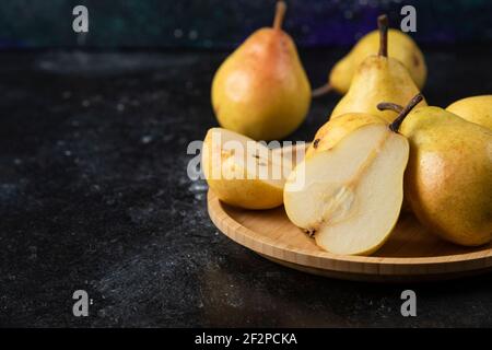 Wooden plate of delicious yellow pears on black surface Stock Photo