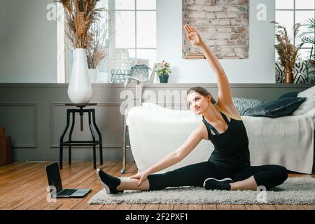 Positive athletic woman with neatly tied hair and tight sportswear stretching   at home. The young woman goes in for sports at home. Stock Photo