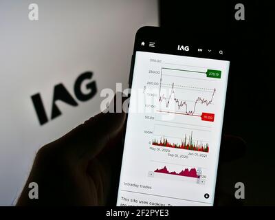 Person holding cellphone with website of company International Airlines Group (IAG) on screen in front of logo. Focus on center of phone display. Stock Photo