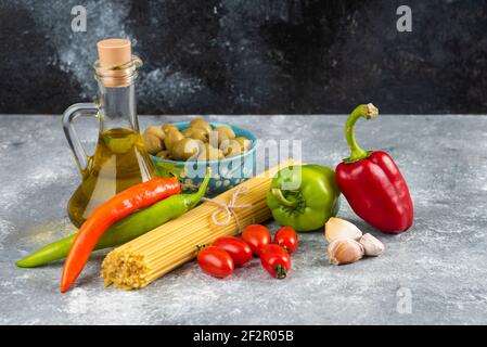 Spaghetti, oil and various vegetables on stone table Stock Photo