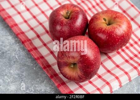 Three red apples with striped tablecloth on marble surface Stock Photo