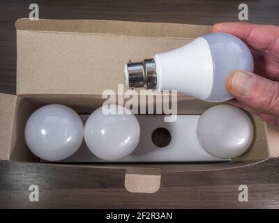 Closeup POV overhead shot of a man's hand removing a new bayonet fitting LED, energy saving light bulb, from a retail box of four bulbs. Stock Photo