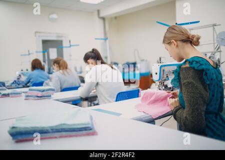 Young beautiful seamstress sews on sewing machine in factory. Stock Photo