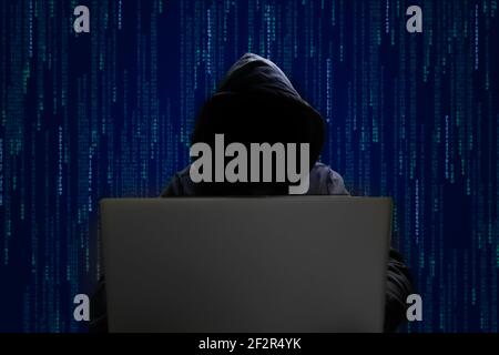 silhouette of a man in a hood working as a hacker at the computer in the dark room at night, hacking the system and laundring secret information. Stock Photo