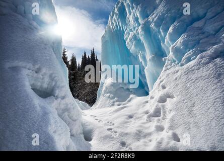 Frozen mountain waterfall with icicles against blue sky and forest at background Stock Photo