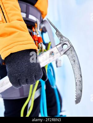 Woman climber is holding vintage ice axe near frozen waterfall in the mountains Stock Photo