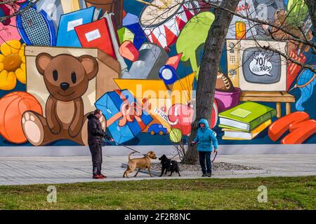 Two people meeting with their dogs in front of the colorfully painted facade of a high-rise building in the center of town. Stock Photo