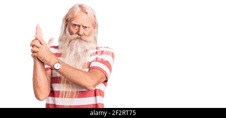 Old senior man with grey hair and long beard wearing striped tshirt holding symbolic gun with hand gesture, playing killing shooting weapons, angry fa Stock Photo