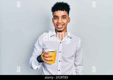 Young african american man drinking a cup of coffee looking positive and happy standing and smiling with a confident smile showing teeth Stock Photo