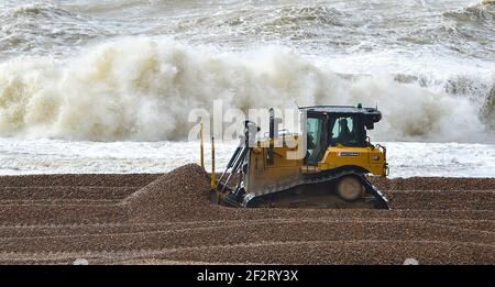 Brighton UK 13th March 2021 - Workmen shift shingle along the beach by Brighton Marina as strong winds batter the south coast again today : Credit Simon Dack / Alamy Live News Stock Photo