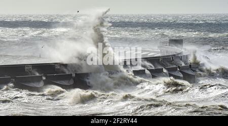 Brighton UK 13th March 2021 - Waves crash over Brighton Marina as strong winds batter the south coast again today : Credit Simon Dack / Alamy Live News Stock Photo