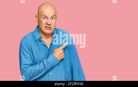 Middle age bald man wearing casual clothes pointing aside worried and nervous with forefinger, concerned and surprised expression Stock Photo