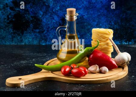 Various pasta, oil and vegetables on wooden board Stock Photo