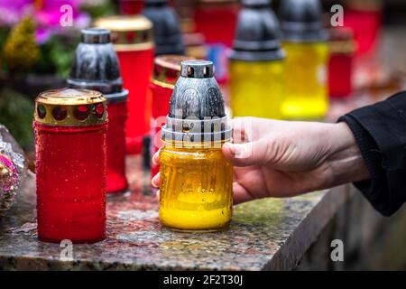 Woman is putting candle lantern at grave in cemetery. Grief for dead person. Close-up hand holding lantern at tombstone Stock Photo