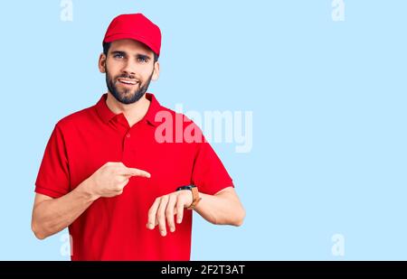 Young handsome man with beard wearing delivery uniform in hurry pointing to watch time, impatience, upset and angry for deadline delay Stock Photo