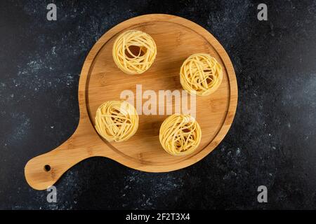 Uncooked pasta nests on wooden board top view Stock Photo