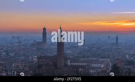 Beautiful panoramic sunset view of old town of Verona, Torre Lamberti and Santa Anastasia bell tower covered with evening fog. View from Piazzale Cast Stock Photo