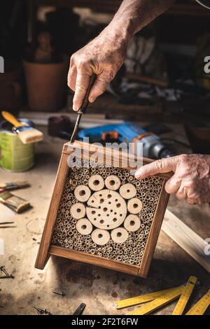 Man making wooden insect hotel. Craftsperson working in his workshop. Old hands screw wood insect shelter house Stock Photo