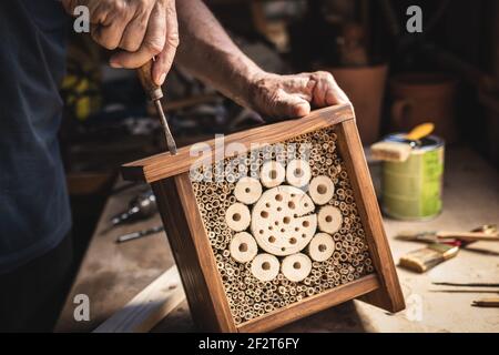 Man making wooden insect hotel. Craftsperson working in his workshop. Old hands screw wood insect shelter house Stock Photo