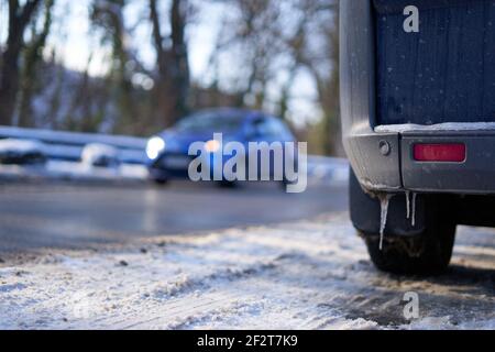 Reflector and sensor of a vehicle, icicles hanging, car standing on snowy and slippery road, blue car out of focus in the background. Parking and driv Stock Photo